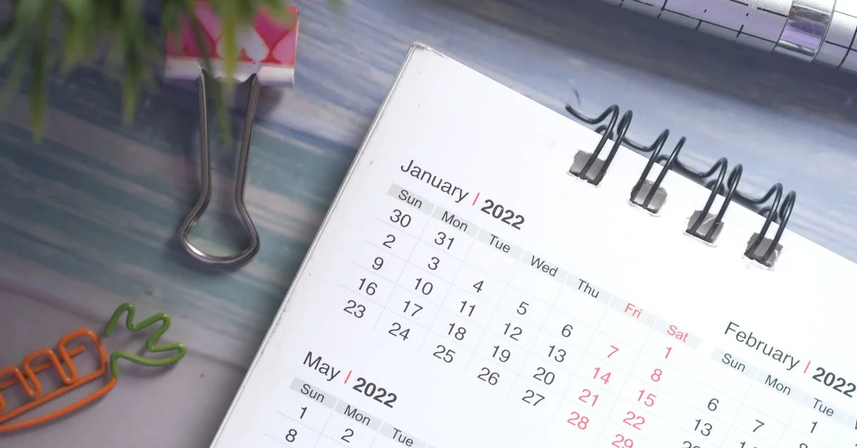 Un calendrier de bureau 2022 avec des clips colorés et un stylo sur un bureau en bois.
