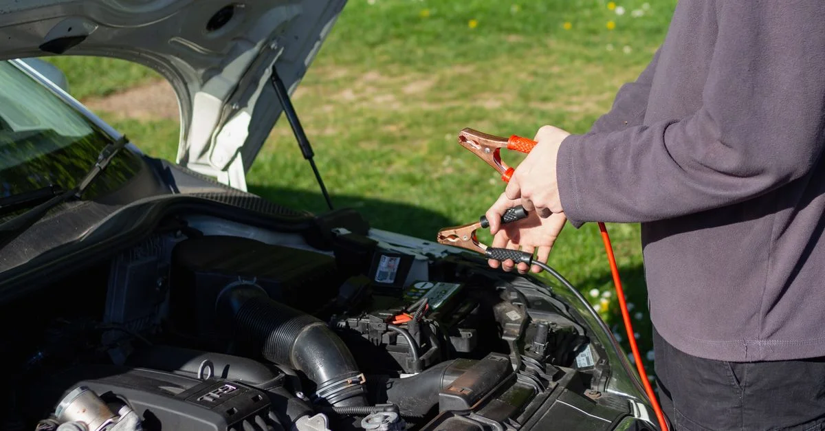 Homme utilisant des câbles de démarrage sur le moteur d'une voiture en plein air par une journée ensoleillée. Concept d'entretien et de réparation de véhicule.